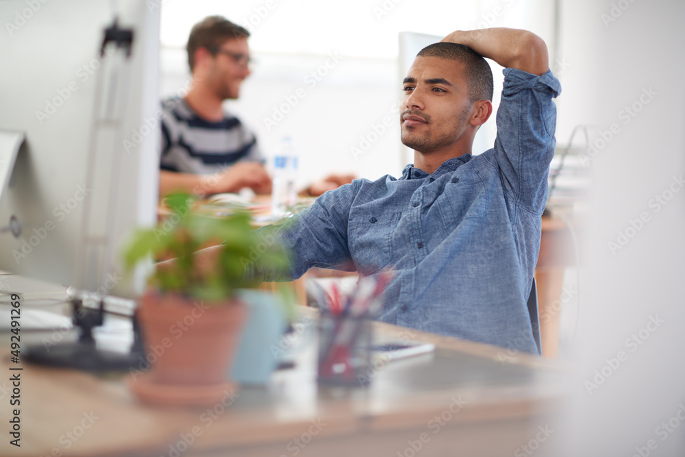 Poster Trouble shooting modern problems. Serious young multi-ethnic man working at his desk in an open plan work space.