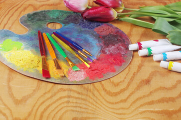 Art palette, brushes, paints, tulips on a wooden texture background. Copy space.