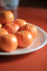 Small oranges are placed in a white plate on the orange table.