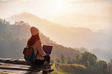 Young woman freelancer traveler working online using laptop and enjoying the beautiful nature landscape with mountain view at sunrise - obrazy, fototapety, plakaty