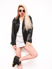 Young beautiful confident female in trendy summer evening silver dress. Sexy carefree blond  woman posing near white wall in studio. Model in black leather biker jacket and red lips. In sunglasses