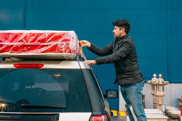 Man arranging mattress on top of the car. Shopping concept