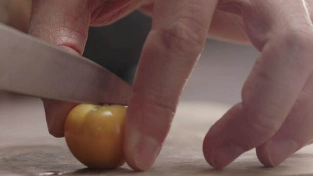 Slow motion man cut physalis in halves on wood board