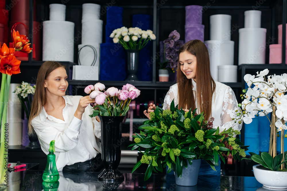 Wall mural two young women take orders by phone and make beautiful festive bouquets in a cozy flower shop. flor