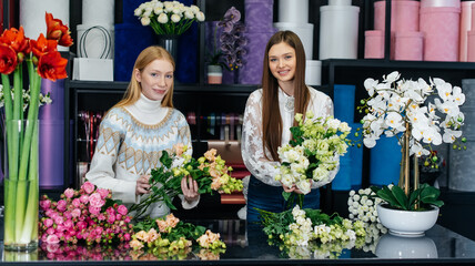 Two young women take orders by phone and make beautiful festive bouquets in a cozy flower shop. Floristry and bouquet making in a flower shop. Small business.