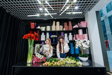 Two young women take orders by phone and make beautiful festive bouquets in a cozy flower shop. Floristry and bouquet making in a flower shop. Small business.