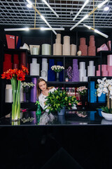 A young female florist takes care of flowers in a cozy flower shop and collects bouquets. Floristry and making of bukets in a flower shop. Small business.