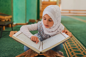 Child girl reading a holy book Quran in the mosque