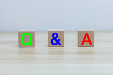 Three wooden cubes with the letters Q and A on the surface of a wood table. short for question and...