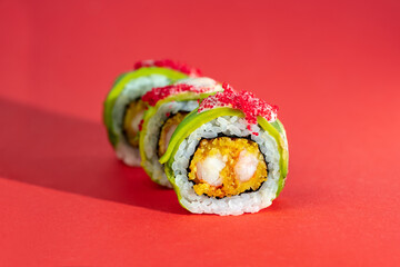 Set of sushi roll with shrimp, avocado and flying fish caviar on red background. Creative image on...