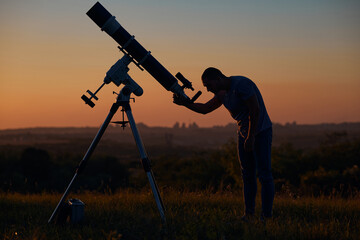 Silhouette of a man, astronomical telescope and countryside.