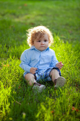 Portrait of a little baby boy sitting on grass playing outdoor in the grass.