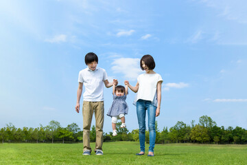 青空を背景に緑の芝の広場で手を繋ぎ遊ぶ幸せな親子3人。家族,愛情,幸せなイメージ