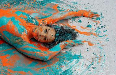 Head and upper body of expressive sexy naked woman lying elegant on the floor in turquoise blue orange color abstractly painted torso bodypainting woman on the splashed ground - obrazy, fototapety, plakaty