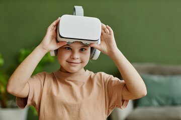 Waist up portrait of cute girl with down syndrome enjoying VR at home and looking at camera, copy...