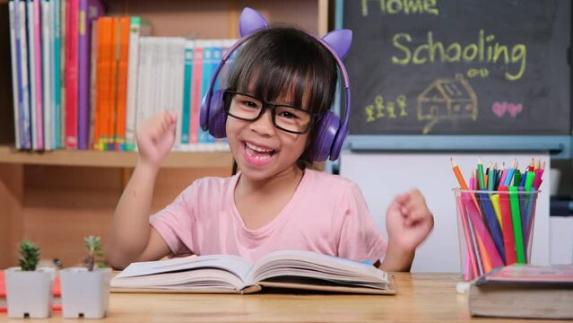 Cute little girl with headphones listening to audiobooks and looking at English learning books on the table. Learning English and modern education