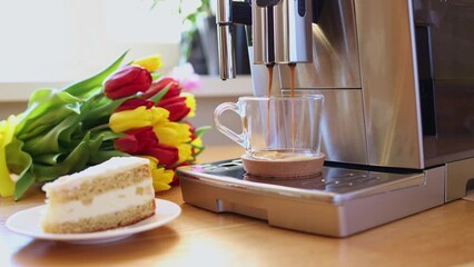 Cup of coffee with milk, piece of cake and tulips flowers on wooden kitchen table. Freshly brewed Americano espresso in coffee machine for breakfast. Stylish home interior decor. High quality 4k