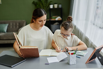 Front view portrait of young female tutor or mother helping girl with down syndrome studying at home together