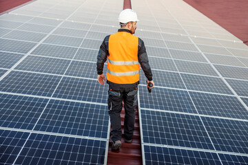 A worker walking around roof between solar panels and preparing to fix it.