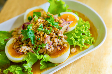 Spicy salad with boiled egg in white dish on wood table