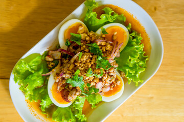 Spicy salad with boiled egg in white dish on wood table