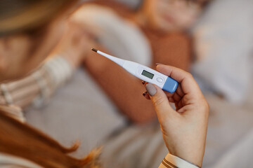 Closeup of unrecognizable mother holding thermometer while caring for sick child at home, copy space