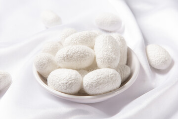 The silkworm cocoon in plate on white silk fabric.