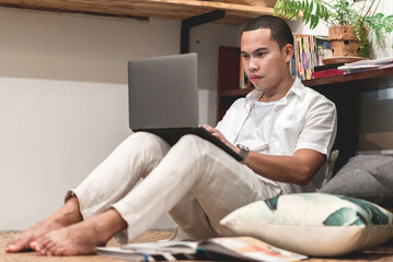 Asian man sitting with his knees bent and using a laptop computer