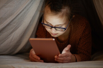 Obraz premium Portrait of young girl with down syndrome using smartphone in bed hiding under covers, digital obsession