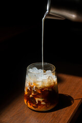 Ice coffee on a wooden table with cream being poured into it showing the texture and refreshing look of the drink