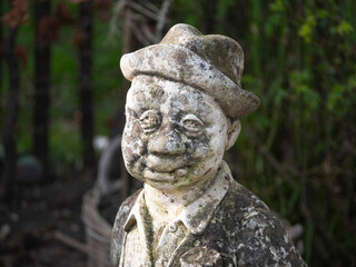 Close up photo of a hard weathered concrete statue, man in suit with hat