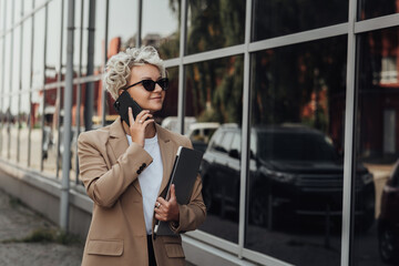 Fototapeta premium Modern Business Lady Smile and Talking on the Phone When Holding Laptop Outdoors