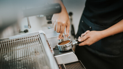 Barista using a tamper to press ground coffee into a portafilter. Close-up view on barista hands to making coffee with coffee machine. Coffee owner concept.