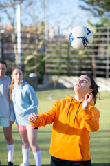 Female football players enjoying training outdoors. One of four girls in sportswear playing ball trying to hit it with head and her girlfriends looking at her. Healthy lifestyle and team sport concept