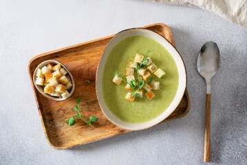Bowl of broccoli cream soup with parmesan cheese, crunchy croutons and microgreen on a wooden tray,...