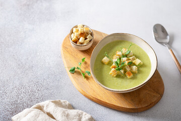 Green vegetable cream soup in a white bowl on a gray concrete background top view. Vegan soup puree of green vegetables. Vegetarian and diet food. Bowl of broccoli cream soup. Copy space