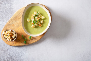 Fresh broccoli soup with croutons and micro green in a bowl on gray background. Spring vegan recipe, healthy food, detox, menu. Top view, copy space