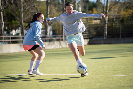 Happy girls playing football on sunny day. Two young girls in sportswear focused on playing, running on green field and enjoying kicking ball. Healthy lifestyle and womens football concept - Powered by Adobe