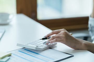 Fototapeta premium female accountant using calculator and typing on laptop. finance accounting plan concept