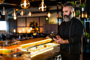 Portrait of sushi chef at sushi restaurant. He is receiving order on digital tablet.