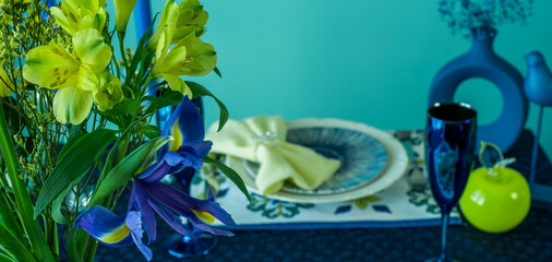 Table setting in blue and yellow colors. On a dark tablecloth a plate, a vase of flowers and decor