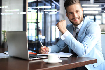 Fototapeta na wymiar Portrait of happy businessman sitting at office desk, looking at camera, smiling