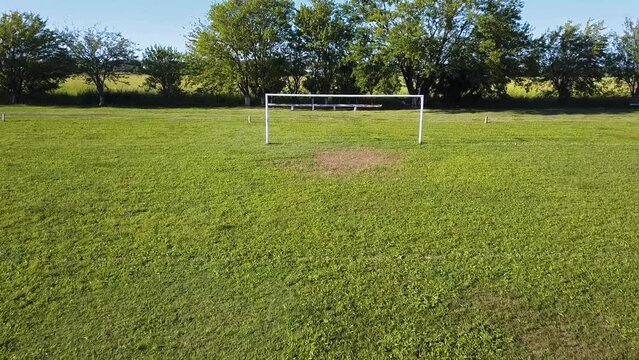 Empty soccer field and goal with green grass. Nature in the background. Concept of outdoor sport. Drone Low Aerial Push In