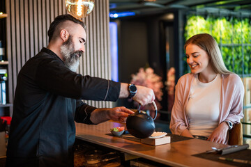 Sushi master is serving sushi meal to cheerful young woman at sushi restaurant.