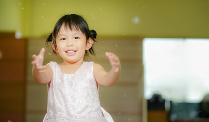 Happy Little girl playing soap bubbles in living room.