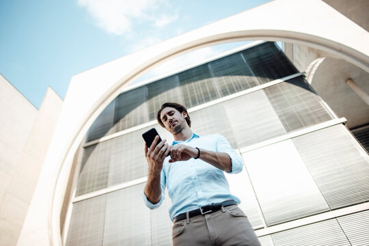 Businessman text messaging through mobile phone in front of modern building