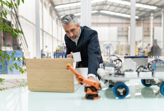 Businessman holding coffee cup looking at laptop in factory