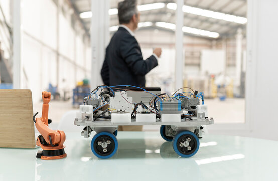 Model of robotic arm and vehicle on desk with businessman standing in background at factory