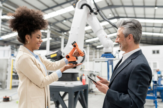 Smiling developer showing model of robotic arm to businessman in factory