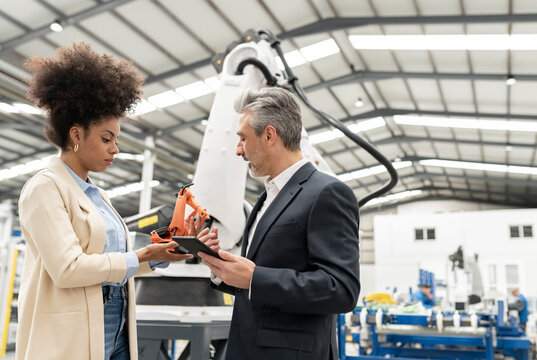 Engineer holding tablet PC explaining about robotic arm to developer in factory